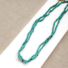 Turquoise beaded necklace on a white and beige fabric background