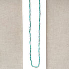 Long turquoise beaded necklace on a beige fabric background