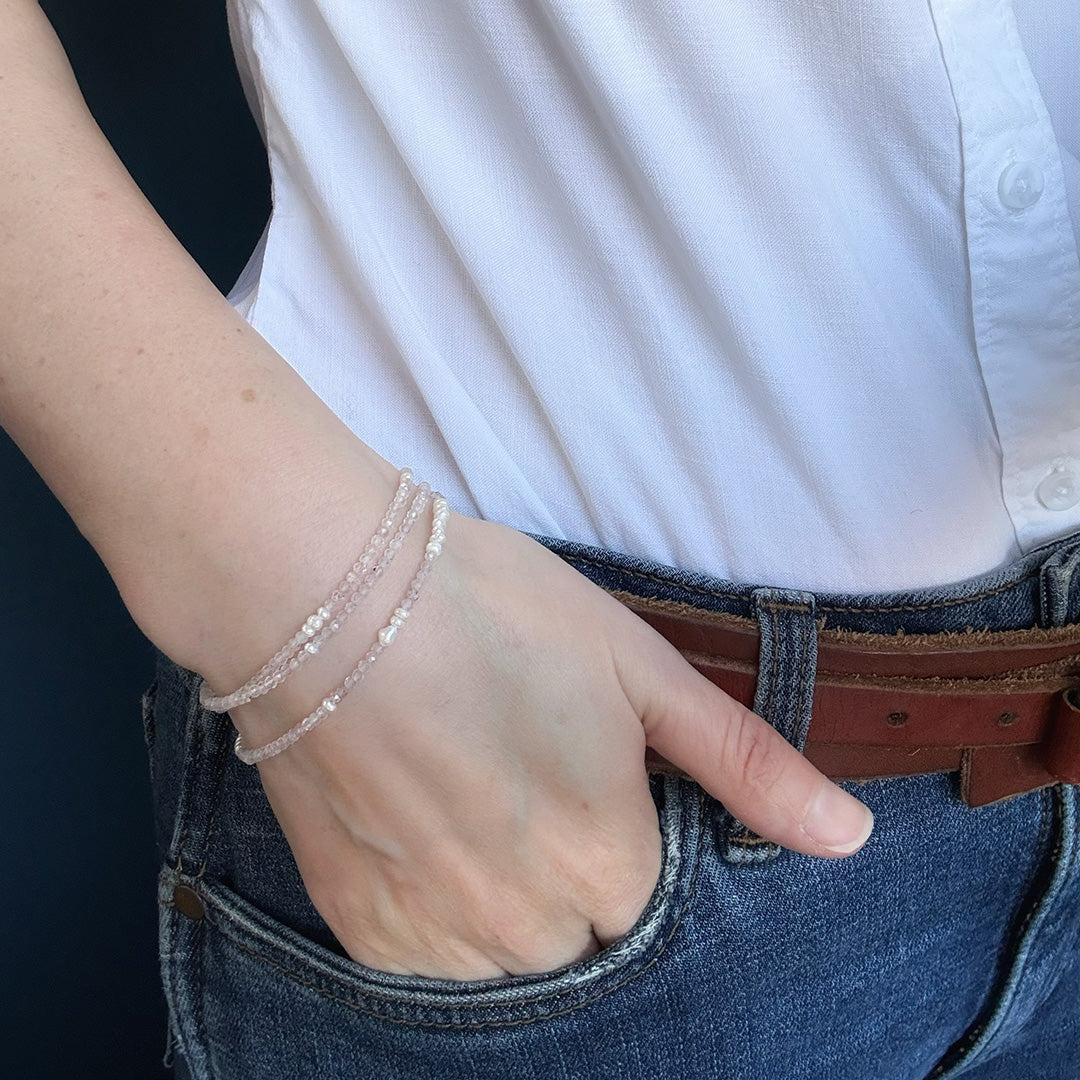 Person wearing a white shirt and blue jeans with option 1 bracelet on a dark background