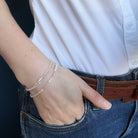 Person wearing a white shirt and blue jeans with option 1 bracelet on a dark background