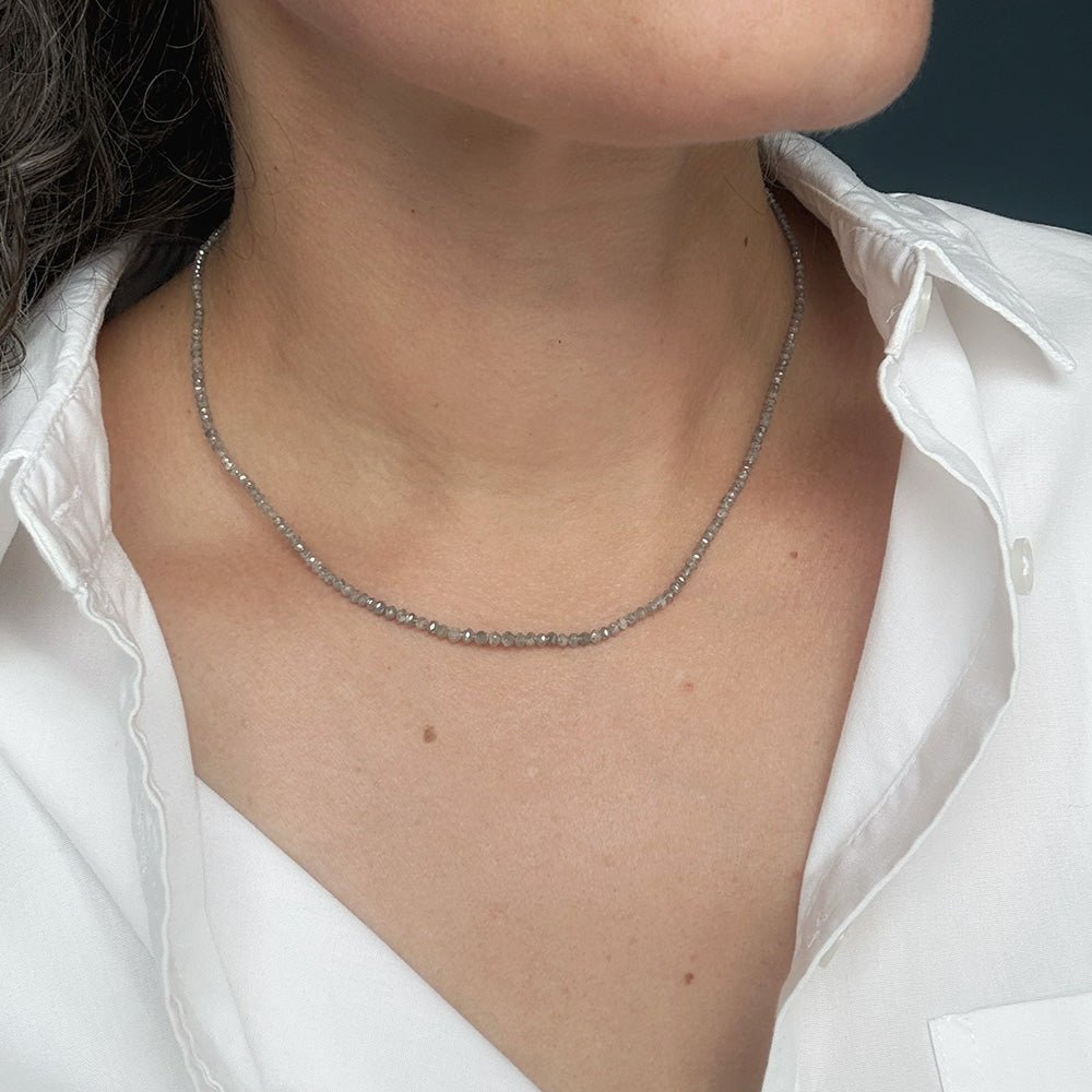 A close-up of a person wearing a delicate rough cut diamond  strung necklace over a white collared shirt.
