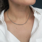A close-up of a person wearing a delicate rough cut diamond  strung necklace over a white collared shirt.
