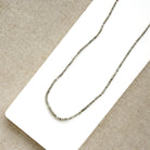 A delicate rough cut diamond strung necklace draped over a white rectangular display card, set against a textured beige fabric background.