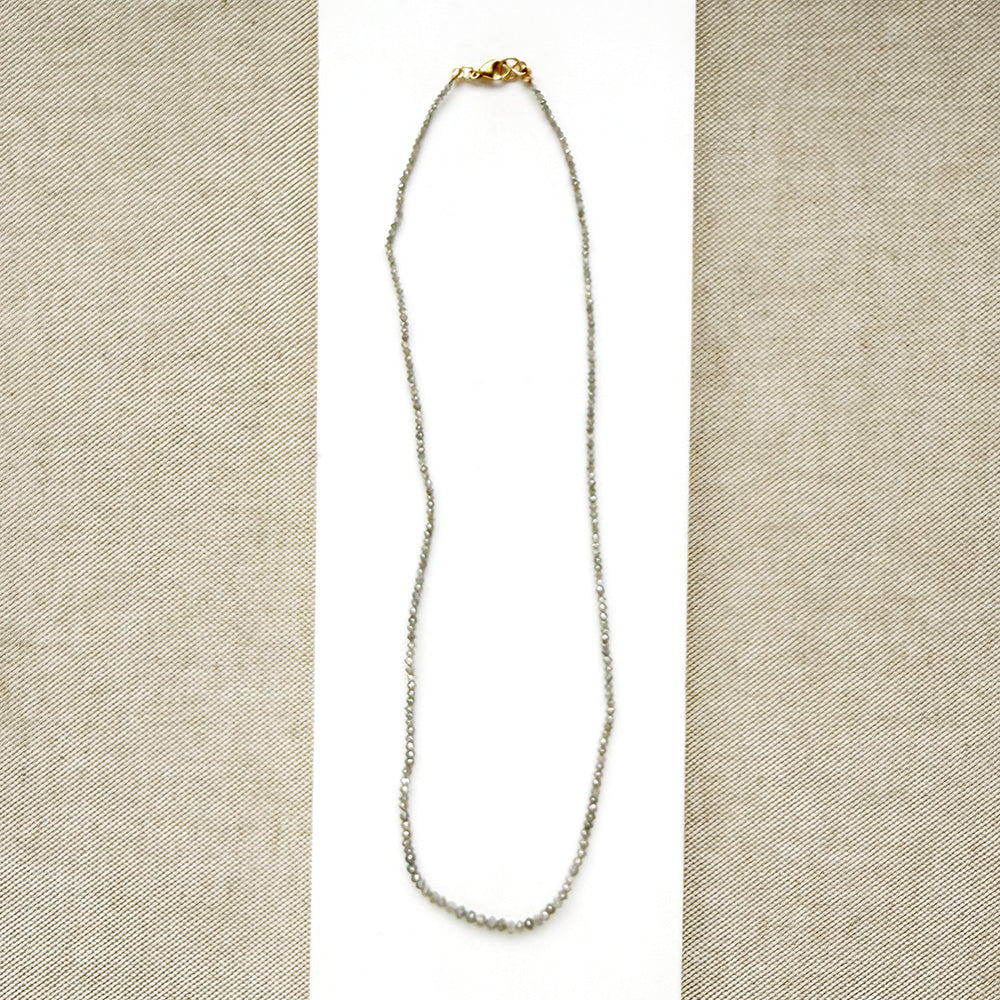 A delicate rough cut diamond strung necklace draped over a white rectangular display card, set against a textured beige fabric background.