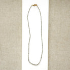 A delicate rough cut diamond strung necklace draped over a white rectangular display card, set against a textured beige fabric background.