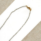 A delicate rough cut diamond strung necklace draped over a white rectangular display card, set against a textured beige fabric background.