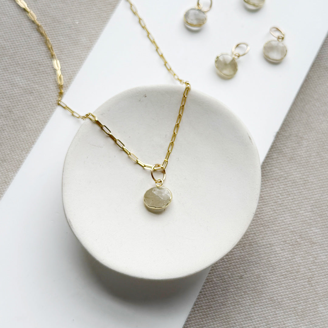 Rutilated quartz charm on a gold chain in a white dish