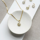 Rutilated quartz charm on a gold chain in a white dish