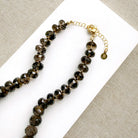 A knotted necklace of faceted smokey quartz gemstones resting on a white dish. The necklace features a gold-tone lobster clasp and extender chain.
