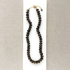 A knotted necklace of faceted smokey quartz gemstones resting on a white card. The necklace features a gold-tone lobster clasp and extender chain.
