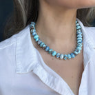 Close up of golden hills necklace with blue beads worn by a person in a white shirt
