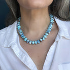 Close up of golden hills necklace with blue beads worn by a person in a white shirt
