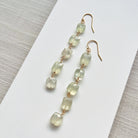 Green beaded earrings on a white card with a gray textured background