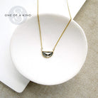 Solid gold necklace with a half moon salt and pepper diamond pendant on a white dish, branded 'One of a Kind'.