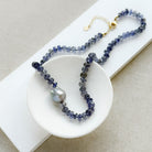 Knotted iolite gemstone necklace with gray baroque pearl in a white dish