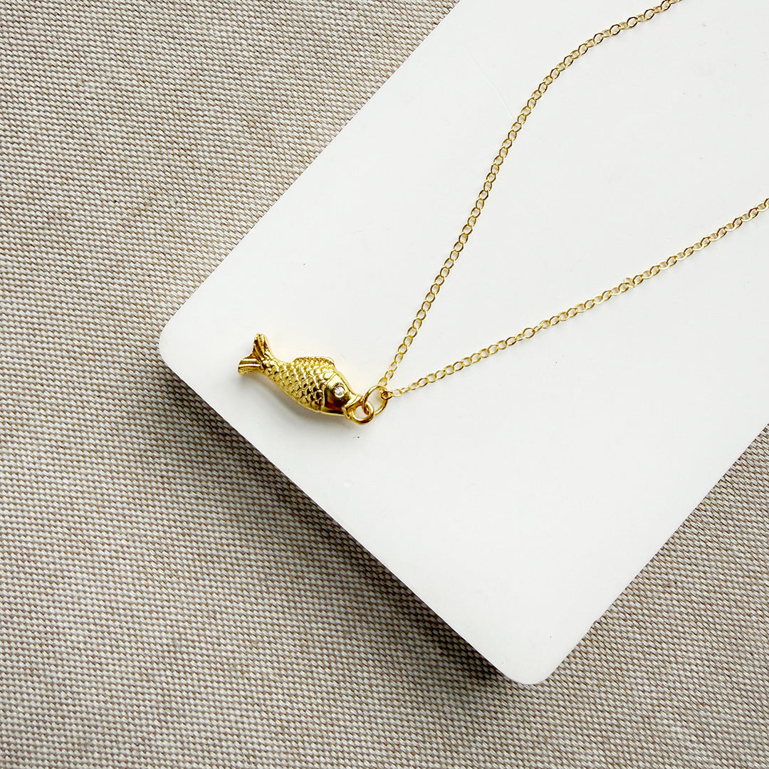 Gold fish-shaped pendant on a chain against a beige background