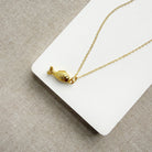 Gold fish-shaped pendant on a chain against a beige background