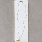 Gold fish-shaped pendant on a chain against a beige background