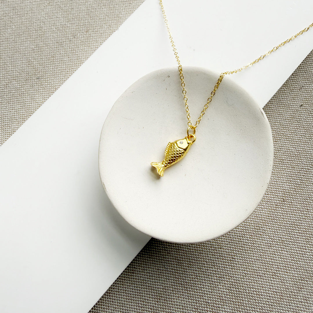 Gold fish-shaped pendant on a chain in a white dish