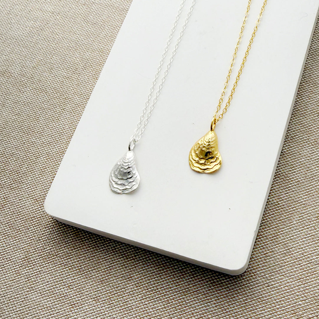Two necklaces with shell pendants, one silver and one gold, on a white card.