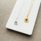 Two necklaces with shell pendants, one silver and one gold, on a white card.
