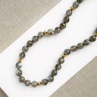 A necklace with round labradorite gemstones, featuring gold disc bead accents, knotted on silk, displayed on a white surface.
