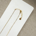 Clasp detail of necklace with blue topaz gemstones and gold chain on a white surface