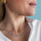 Close up of woman wearing a blue topaz gemstone necklace and earrings against a light blue background