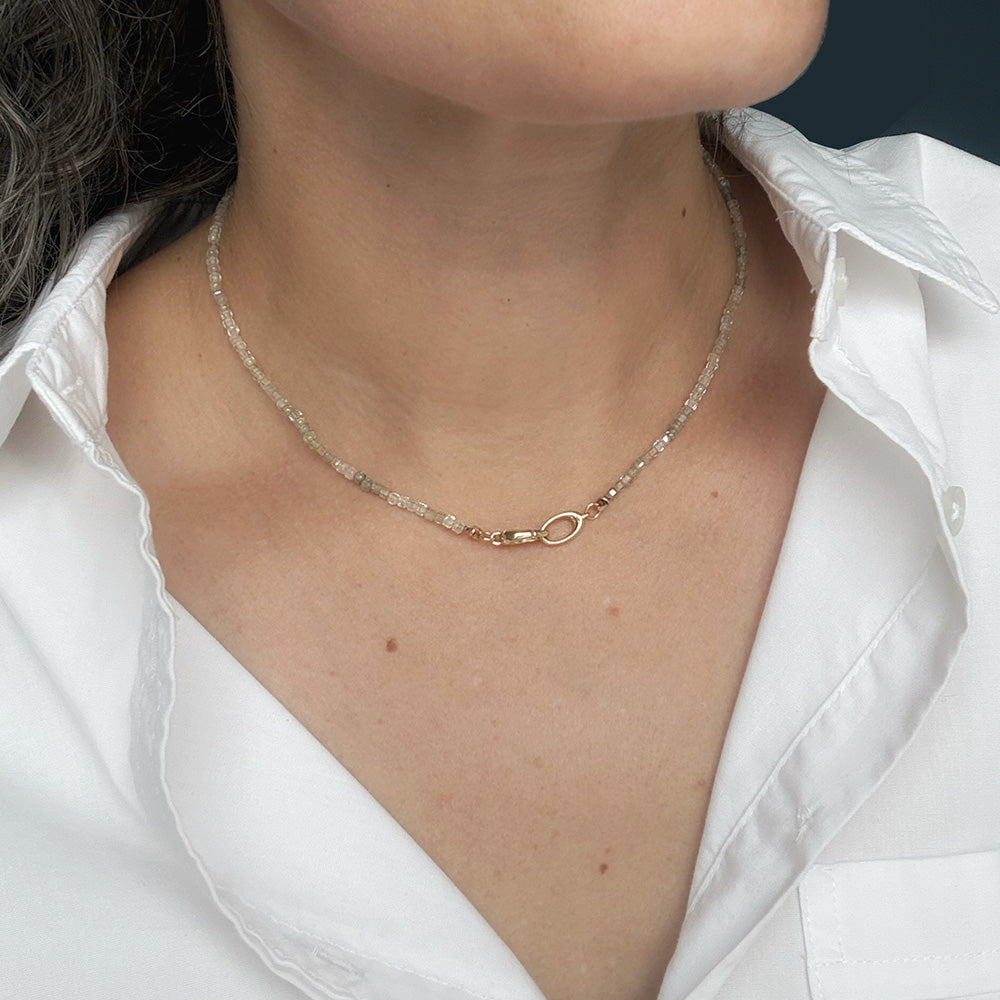 A close-up of a person wearing a delicate white zircon beaded necklace , styled with a white collared shirt.