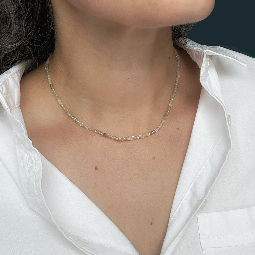 A close-up of a person wearing a delicate white zircon beaded necklace , styled with a white collared shirt.