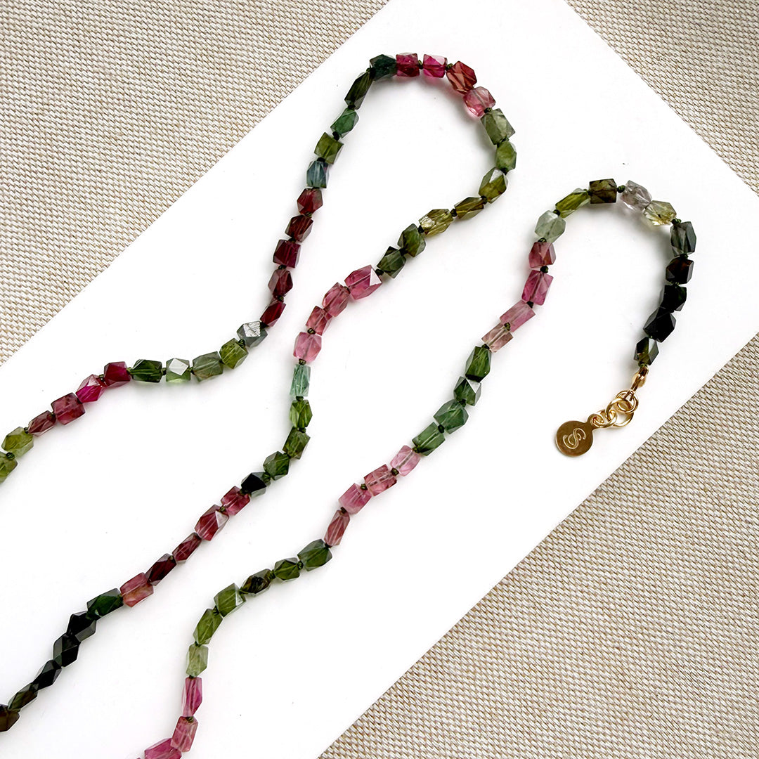 A long strand of knotted watermelon tourmaline, arranged on a white surface with textured beige corner accents.