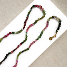 A long strand of knotted watermelon tourmaline, arranged on a white surface with textured beige corner accents.