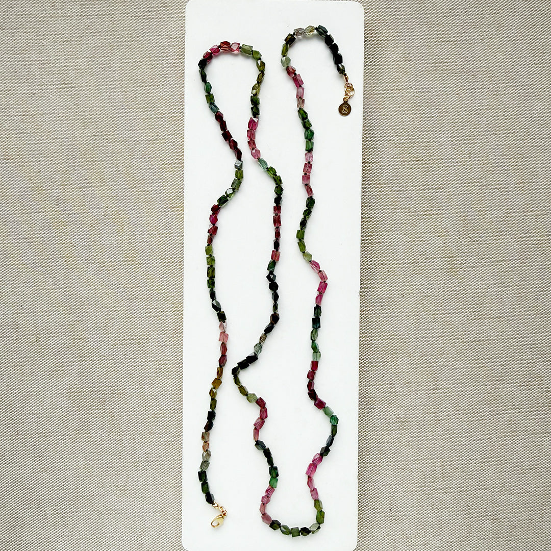A long strand of knotted watermelon tourmaline, arranged on a white surface with textured beige corner accents.