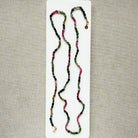 A long strand of knotted watermelon tourmaline, arranged on a white surface with textured beige corner accents.