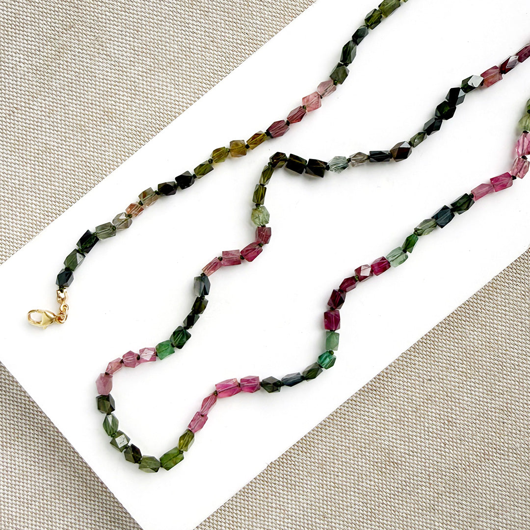 A long strand of knotted watermelon tourmaline, arranged on a white surface with textured beige corner accents.