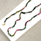 A long strand of knotted watermelon tourmaline, arranged on a white surface with textured beige corner accents.