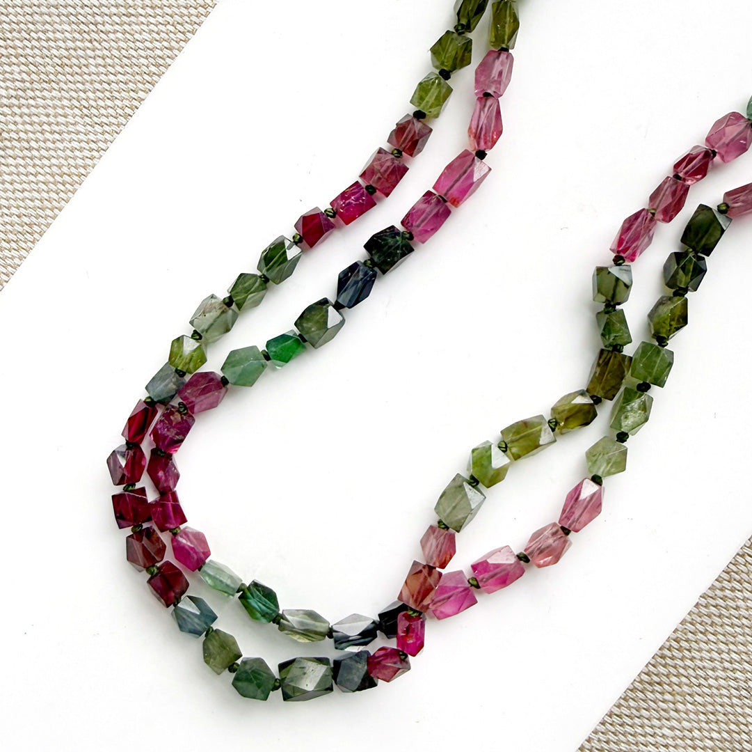 A long strand of knotted watermelon tourmaline, arranged on a white surface with textured beige corner accents.