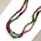 A long strand of knotted watermelon tourmaline, arranged on a white surface with textured beige corner accents.