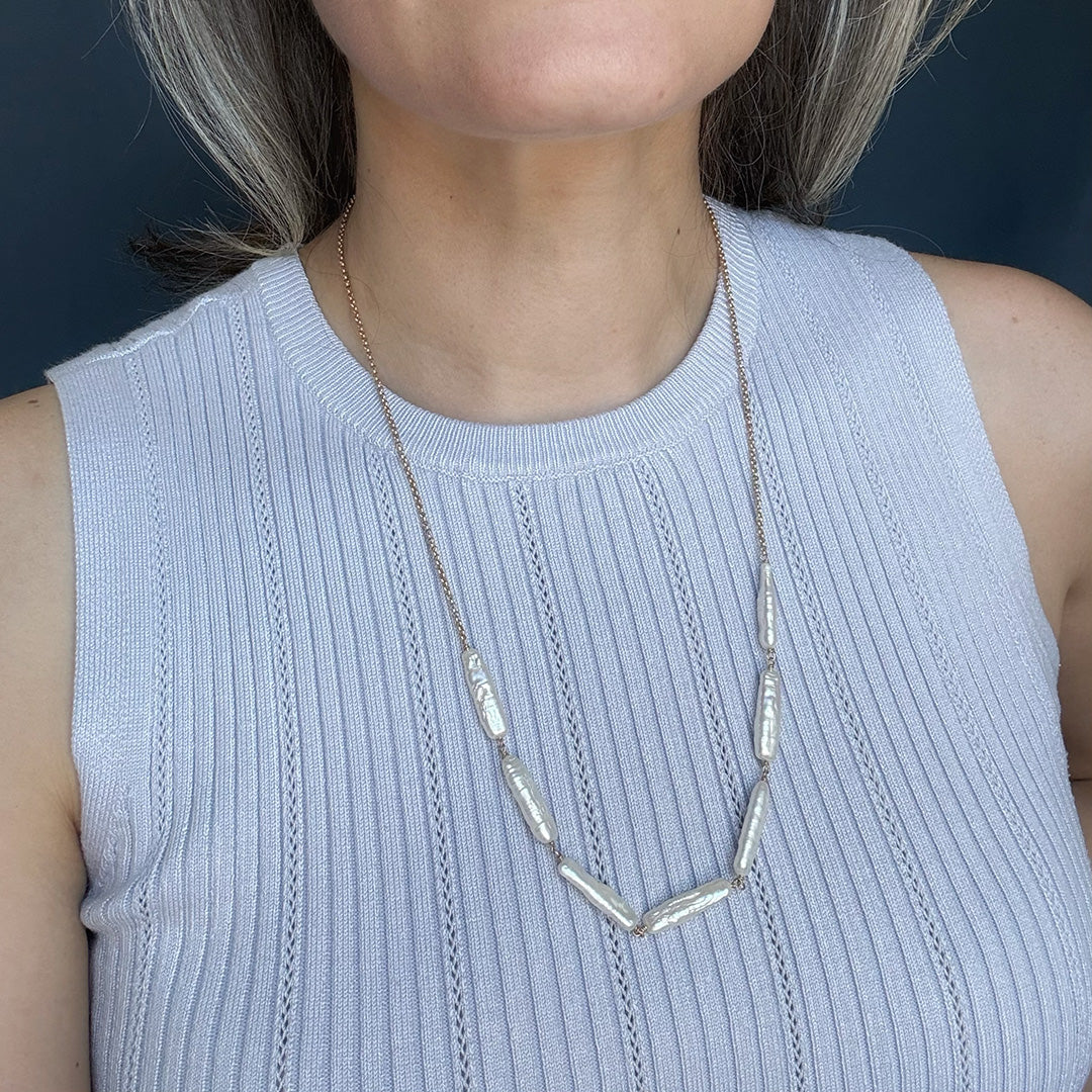 Woman wearing a light blue tank top and stick pearl necklace