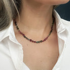 Close up of person wearing a necklace with faceted Watermelon Tourmaline gemstone beads in a multicolor mix of green, pink, and blue, with a white shirt