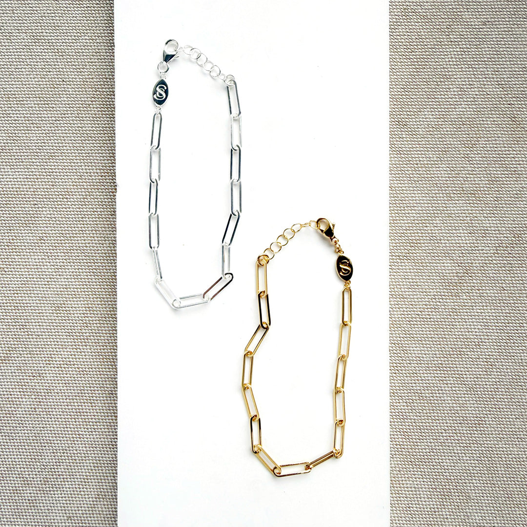 Two chain bracelets, one silver and one gold, on a textured gray background.
