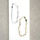Two chain bracelets, one silver and one gold, on a textured gray background.