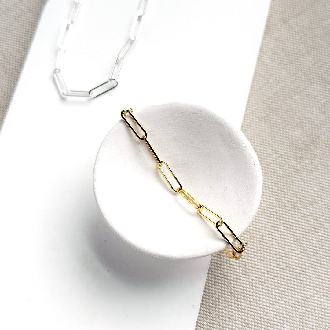 Gold paperclip chain bracelet on a white dish with a neutral background