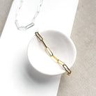 Gold paperclip chain bracelet on a white dish with a neutral background