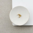 Gold earrings on a white round jewelry dish with a neutral background