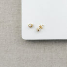 Pair of gold and pearl earrings on a white square platform with a gray fabric background