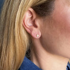 Close-up of a person wearing a pearl and gold stud earring against a blue background