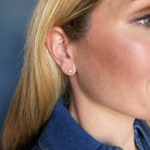 Close-up of a person wearing a pearl and gold stud earring against a blue background