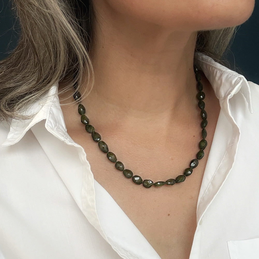 A close-up of a woman wearing a green tourmaline faceted bead necklace with a white collared shirt.