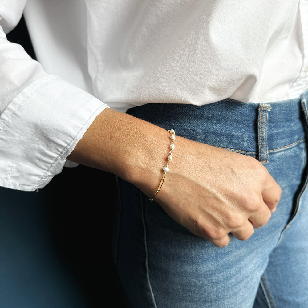 Woman wearing pearl and chain bracelet with a white shirt and jeans 